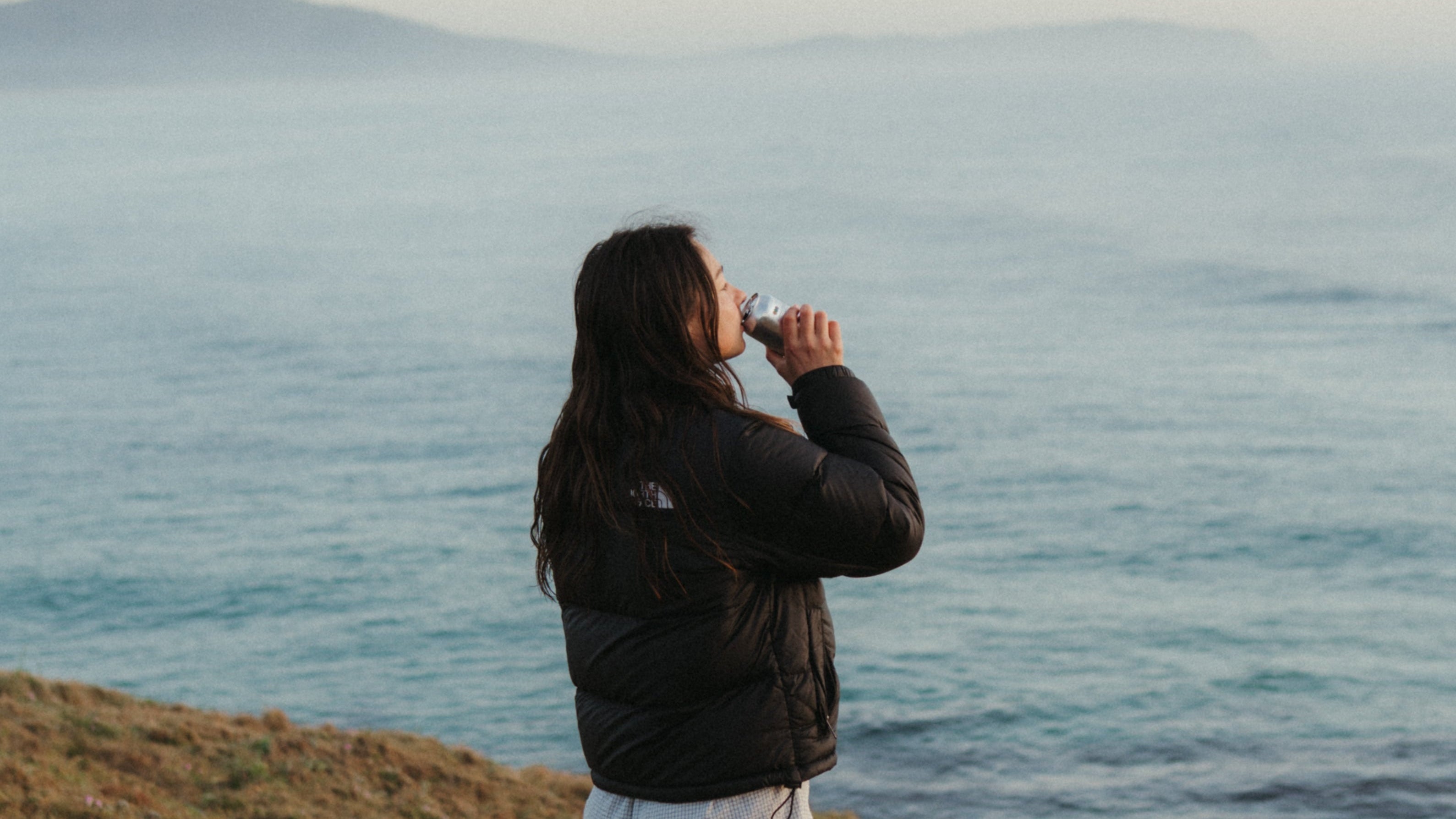 Person standing on a grassy hill overlooking a vast body of water.