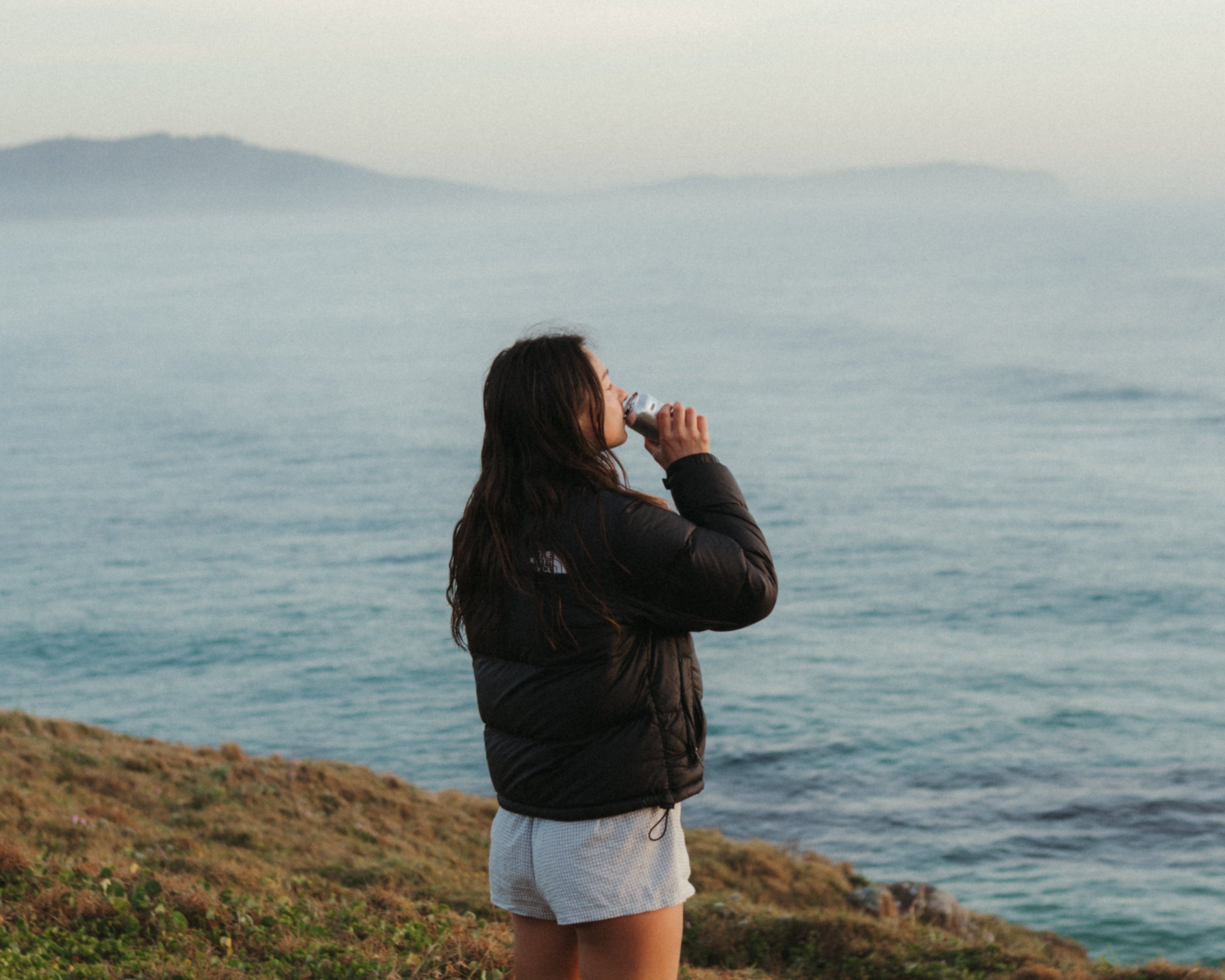 Person standing on a grassy hill overlooking a vast body of water.